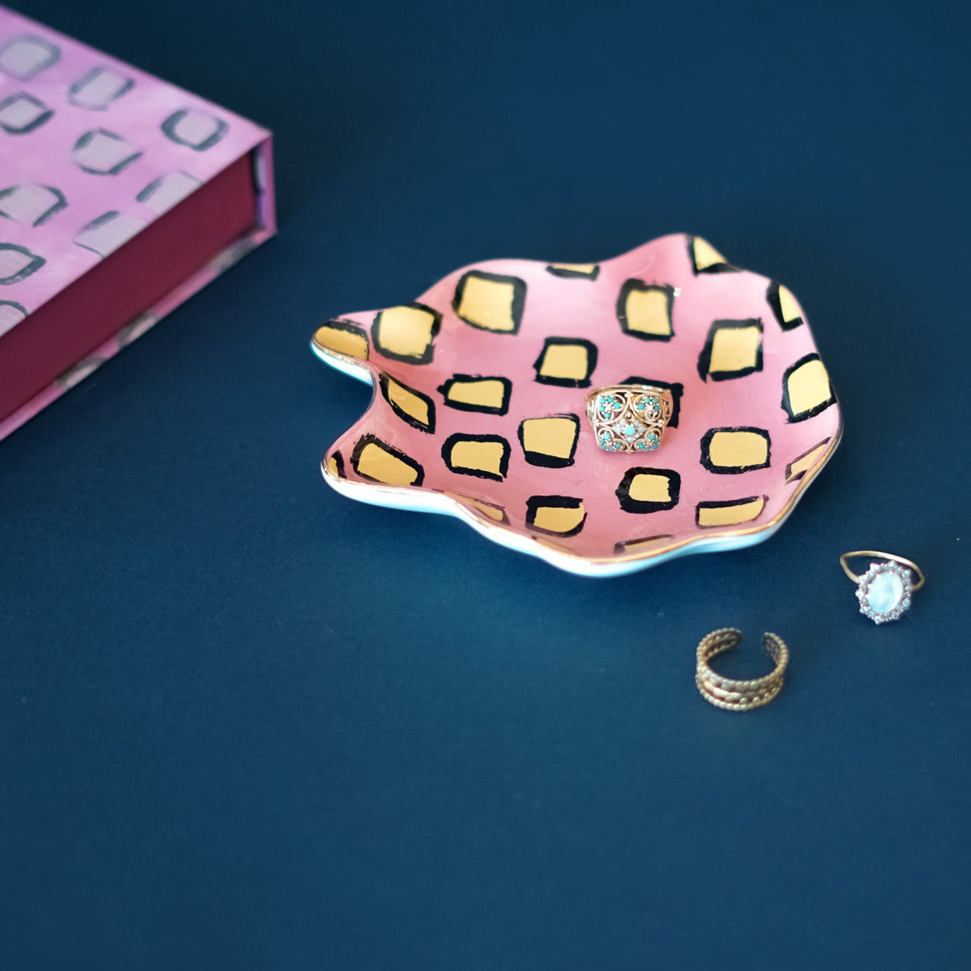 Pink and yellow patterned trinket dish with rings on a blue background