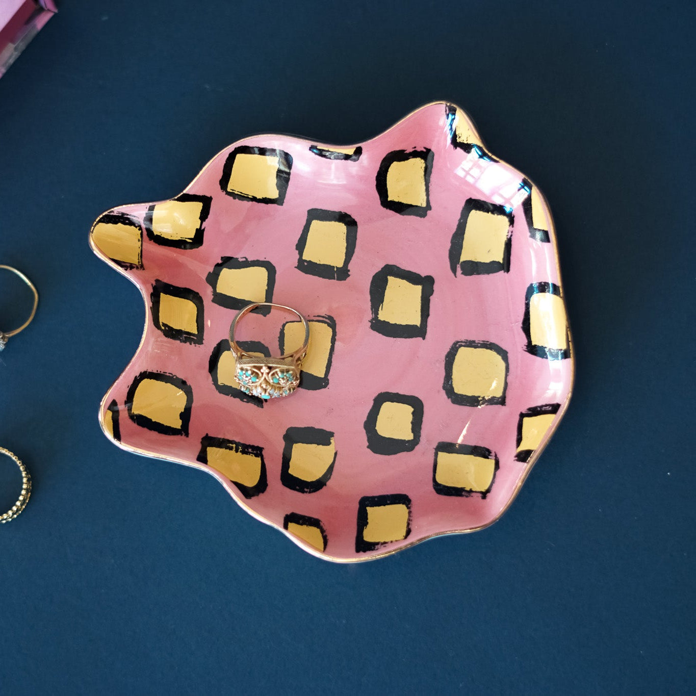 Pink and yellow patterned jewelry dish with rings on a dark blue background