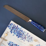 Knife with blue handle on a piece of watercolor art against a dark blue background