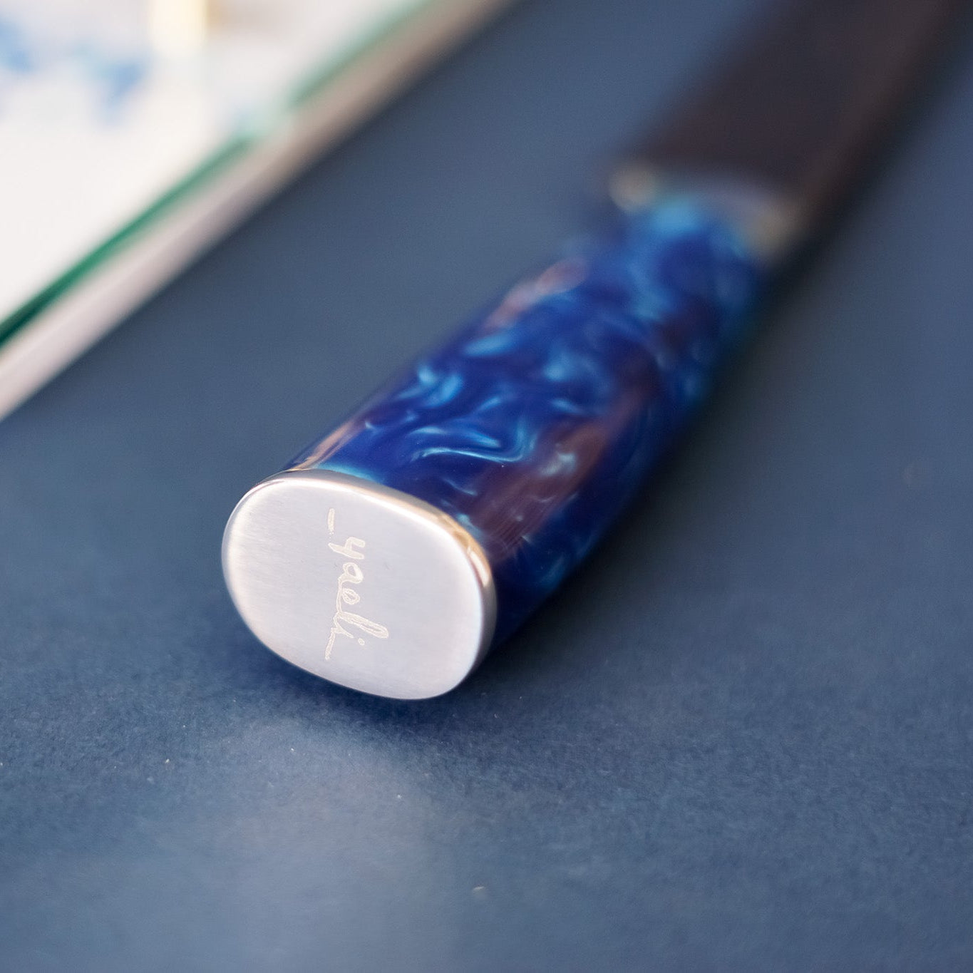 Close-up of a blue and silver knife handle on a blue surface with a blurred board in the background.